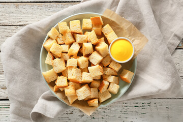 Plate of crunchy croutons and tasty sauce on wooden table, top view