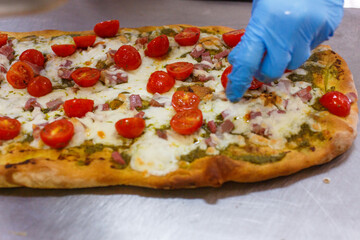 Pizzaiolo mentre termina una pizza romana con sopra pomodori freschi, pesto di basilico, mozzarella di bufala e pancetta