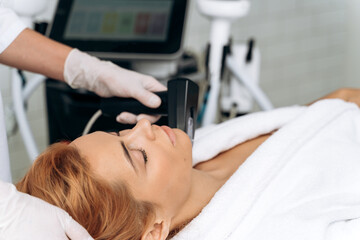 Doctor hands in gloves doing hair removal procedure with appliance for ginger woman