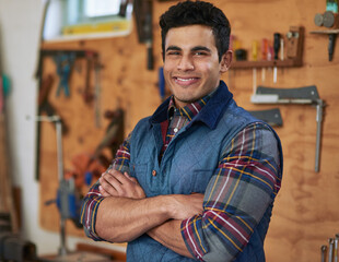 You name it, and I can build it. Portrait of a happy handyman standing in his workshop with his arms folded.