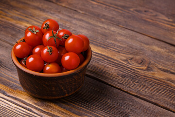 Brown bowl with cherry tomatoes on dark wooden background, selective focus.
