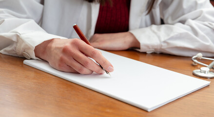 Female doctor hand with a pen on a blank paper, close up, wooden office table, close up view.