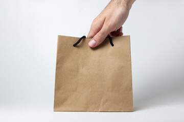 A hand takes a paper bag on a white background. Shopping concept. Eco-friendly paper bag