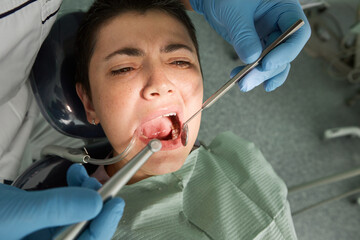 Portrait Of Scared Female Patient Having Terrible Toothache. Dentist Curing Teeth Cavity In Blue...