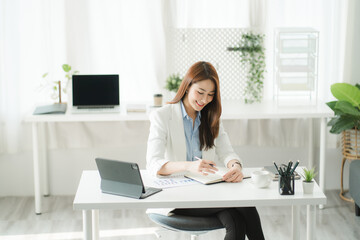 Portraits of beautiful smiling Asian women relax using laptop computer technology while sitting on their desks and using their creativity to work, work from home concept.