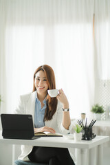 Portraits of beautiful smiling Asian women relax using laptop computer technology while sitting on their desks and using their creativity to work, work from home concept.