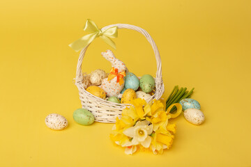 Easter painted eggs in the basket and spring flowers on yellow background. Happy Easter