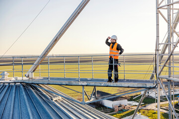 An industry worker looking around while standing on top of the silo.