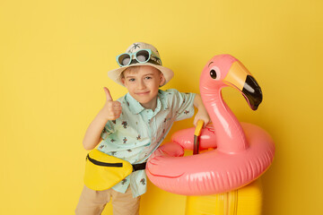 Happy child ready for a summer vacation. Kid having fun against yellow background. Travel and...