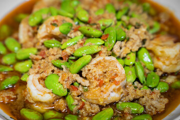 Close up Thai Stir-Fried Stink Beans with Shrimps and spicy shrimp paste sauce in white dish bowl on dark wood table.