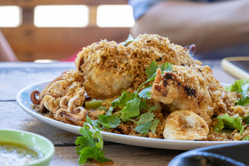 Fried squid with galic and coriander on top in white dish on wood table, ready to eat.