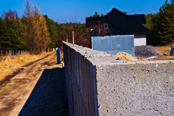 Świeżo zbudowany ( nie wykończony) z bloczków betonowych murek ( ogrodzenie , w okół domu . Na tle nieba błękitnego i lasu .