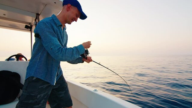 Open sea fishing. Angler stands with fishing rod on the boat floating in the open sea and pulls the fish