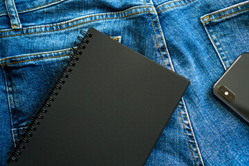 Black notepad and black phone. Denim background.