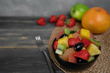 Fresh fruit salad, top view in a bowl on wooden background, vegetarian food concept