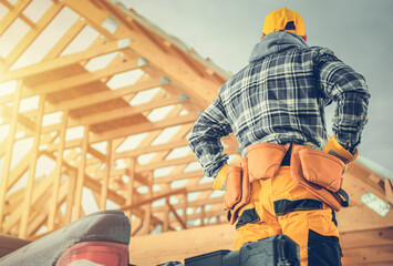 Carpentry Construction Worker in Front of Newly Developed Wooden Skeleton House Frame