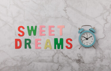 Sleeping eye mask, alarm clock and sweet dreams lettering on marble background. The concept of minimal rest, sleep quality, good night, insomnia, relaxation, sweet dreams. Copy space. Flat lay.