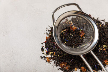 Leaves of black fragrant tea in a brewing strainer and a glass jar on a gray textural background....
