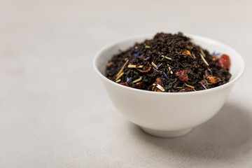 Black tea. Dried black tea leaves in a ceramic bowl. Composition with organic, natural tea on a light background. Place to copy.