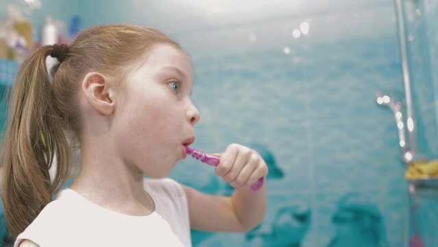 a little six-year-old girl brushes her teeth in the bathroom in front of a mirror, oral hygiene