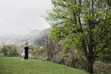 Young pretty emotional caucasian woman with long hair wearing natural makeup in romantic casual clothes walking among spring mountains near the beautiful fresh blooming tree in the countryside.