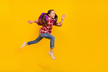 Fototapeta na wymiar Photo of funky cute schoolgirl wear checkered shirt running fast jumping high isolated yellow color background