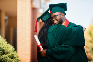 Happy black college student and his female friend hug each other while celebrating their graduation.