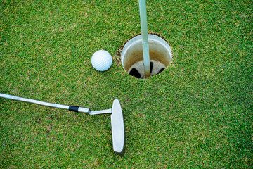 Top view of a golf ball with putter on green course at hole. Golf ball and golf club on green in...