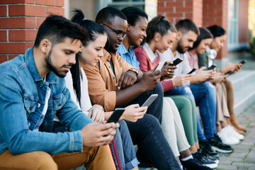 Young black student and his friends using mobile phones while sitting outdoors at campus.