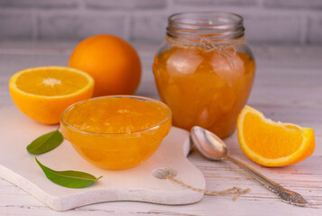 Orange jam in a glass bowl on a white wooden board.