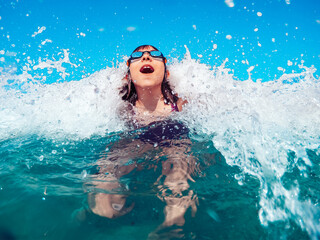 Girl swimming in turquoise water and getting splashed by the wave