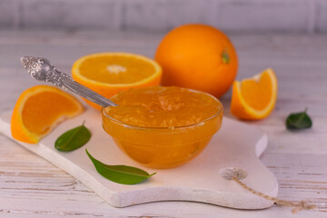 Orange jam in a glass bowl on a white wooden board.