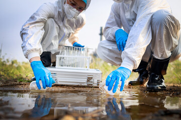 Two Scientists in protective suits and masks took a sample of water for analysis. Environment Issue concept. Environment Issue concept.. - obrazy, fototapety, plakaty