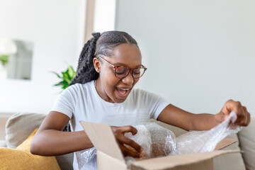 Fototapeta na wymiar Young woman unpack the package she ordered online, African American woman is at home, she unpacks delivered package