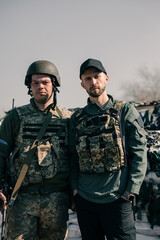Ukrainian territorial defense warrior stands near volunteer on checkpoint in body armor with automatic gun.