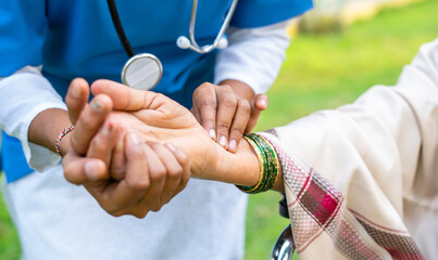 close up shot of Doctor checking pulse rate of womanby holding hand at park - concept of medicare...