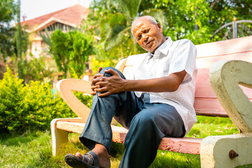 Senior old man suffering from knee joint pain while sitting at park - conept of arthritis,...