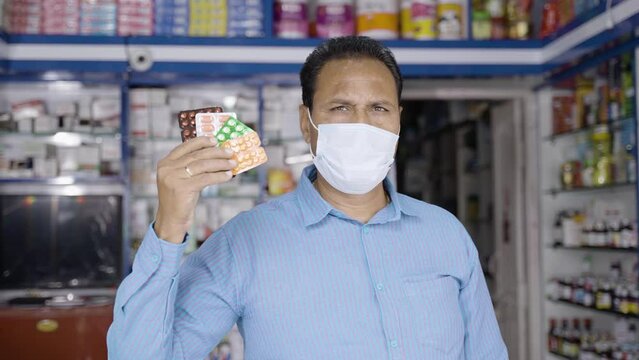 pharmacist with face mask showing stack of pills or medicines at retail medical store - concept of recommendation, healthcare and covid-19 coronavirus protection