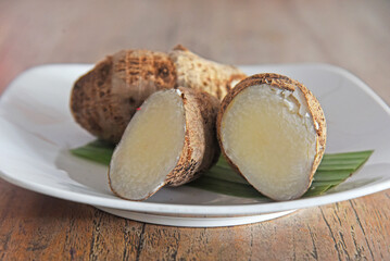Close up of Taro fruits, placed on white plate on wooden background 