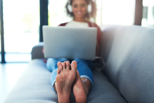Relaxed feet are happy feet. Shot of a young woman using headphones and a laptop on the sofa at home.