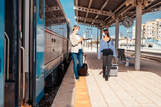 Two happy female friends in protective masks  walking and chatting at train station