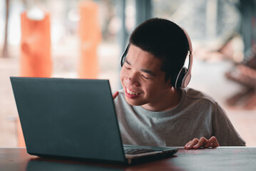 A smart young man with a disability wearing headphones using computer notebook with expression,...