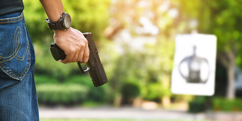 Automatic black 9mm pistol gun holding in hands of shooter and ready to aim to the man-target shooting paper ahead, concept for training and practising human to be body guard and vip protectors.