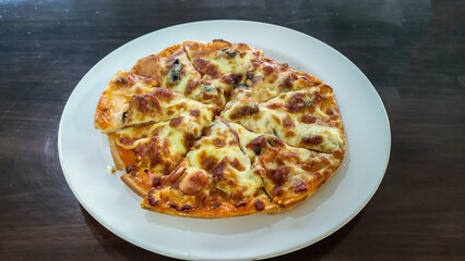 Crispy thin crust pizza with mushroom and sausage on white plate on wooden table