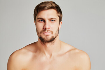 Portrait of a serious young man with bare shoulders on a gray background, powerful swimmers...