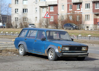 An old blue rusty Soviet car is parked on the street, Badaeva Street, St. Petersburg, Russia, April 2022