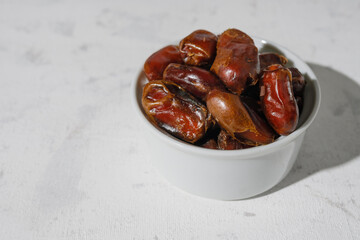 Dried dates in a white cup on a white background. A sunny day.