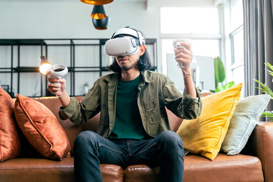 relax casual Asian adult Man Wearing Virtual Reality Headset and Holding Controllers Plays in a sport Video Game at Home. Playing VR active sport game online in the Living Room