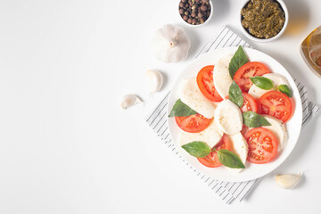 Delicious Italian caprese salad with sliced mozzarella, tomatoes, basil, pesto and garlic on background.