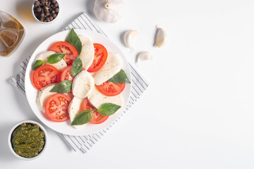 Delicious Italian caprese salad with sliced mozzarella, tomatoes, basil, pesto and garlic on background.